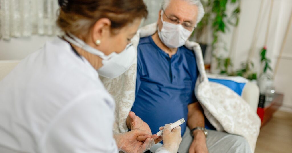 Masked nurse performing a finger-prick blood glucose test on an older man